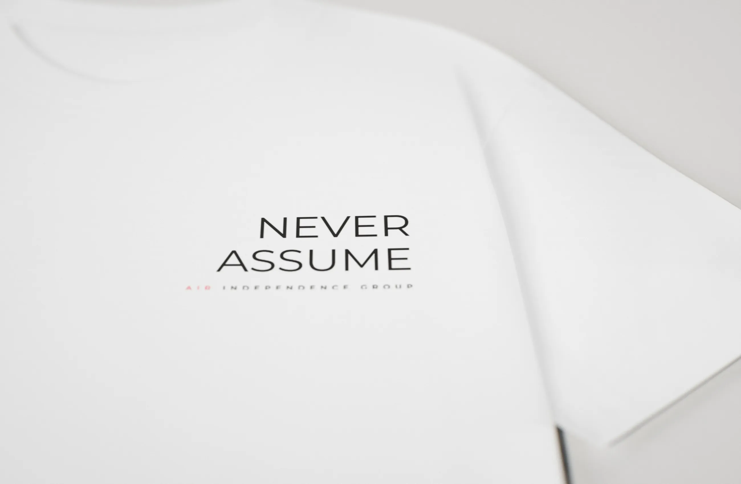 Brustmotiv „Never Assume“ mit dem Namen der Gruppe neben dem Kragen